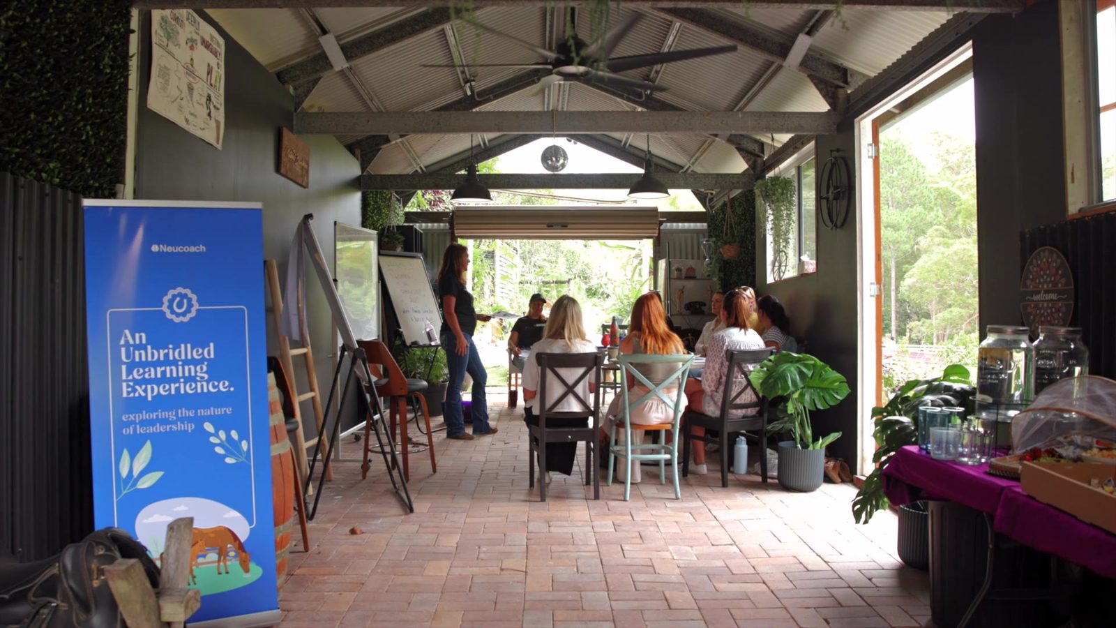 A leadership group seated together in the open-air barn, the Natural Boardroom, with Paula facilitating amid greenery and natural light.